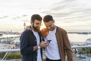 gay Pareja utilizando célula teléfono en Estar atento encima el ciudad con ver a el puerto, Barcelona, España foto