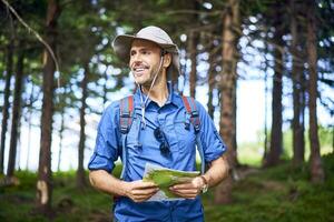 Smiling man holding a map hiking in the forest photo