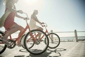 joven hembra amigos ciclismo en paseo a playa durante soleado día foto