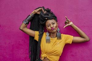 Portrait of woman with long dreadlocks making shaka sign in front of a pink wall photo