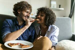 Happy couple sitting on couch eating pizza photo