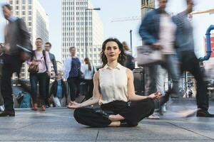 Young businesswoman practising yoga in the city at rush hour, Berlin, Germany photo