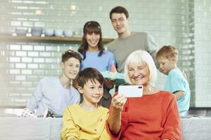 Mother and sons celebrating grandmother's bithday in their kitchen, boy taking selfies photo