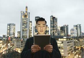 Man using tablet in front of urban skyline at dusk, Frankfurt, Germany photo