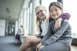 Portrait of two smiling schoolgirls sitting on school corridor photo