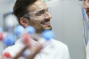 Smiling male scientist holding molecular structure while looking at colleague in illuminated laboratory photo