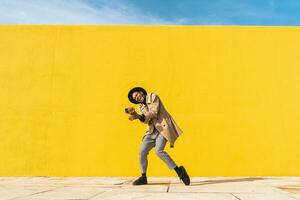 joven hombre bailando en frente de amarillo muro, tomando selfies foto