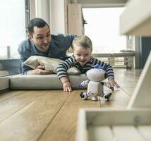 Excited father and son lying on a mattress at home watching a toy robot photo