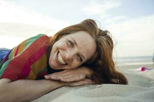 Redheaded woman lying in sand on the beach, with eyes closed photo