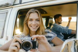 retrato de contento mujer con cámara propensión fuera de ventana de un camper camioneta con hombre conducción foto