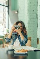 riendo mujer sentado a café tienda tomando imágenes con cámara foto