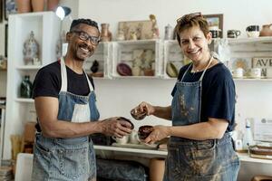 Smiling coworkers holding ceramics while standing in workshop photo