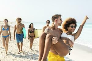 Friends walking on the beach, one man carrying his girlfriend photo