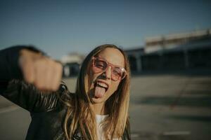 Portrait of young woman outdoors sticking out tongue and punching photo