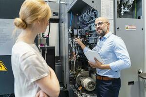 Businessman with tablet showing machine to businesswoman in factory photo