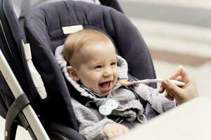 Mother feeding laughing baby boy in stroller photo