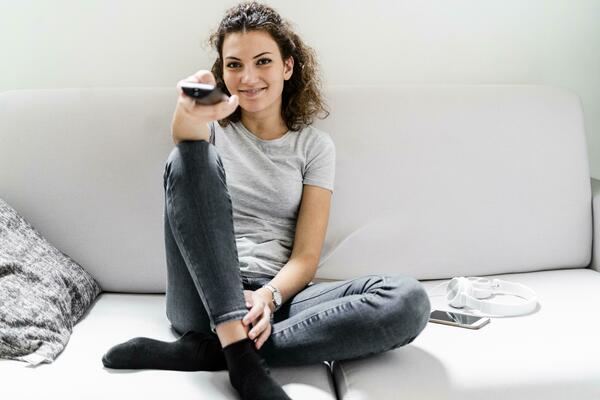 Portrait of smiling young woman sitting on the couch using remote control