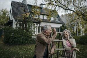 Senior couple with a ladder high fiving in garden of their home photo