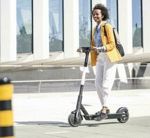 Happy young woman with earphones riding e-scooter in the city photo