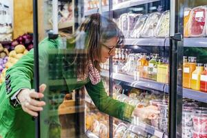 Woman taking packaged berries from cooling shelf in organic store photo