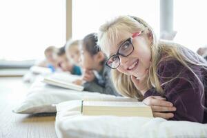 retrato de sonriente Chica de escuela acostado en el piso con compañeros de clase leyendo libro en colegio descanso habitación foto