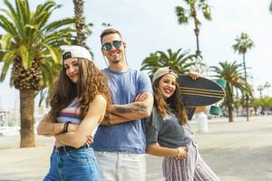 Three happy friends posing with skateboard on a promenade with palms photo