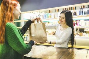 Smiling shop assistant handing over paper bag to customer in a cosmetics shop photo