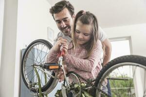 joven hombre y pequeño niña reparando bicicleta juntos foto