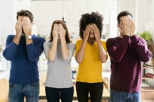 Four friends standing side by side at home covering their faces photo