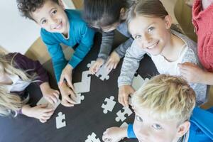 Portrait of smiling pupils playing jigsaw puzzle in school together photo