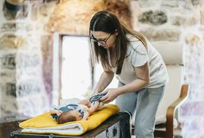 Mother changing diaper of baby while sitting at home photo