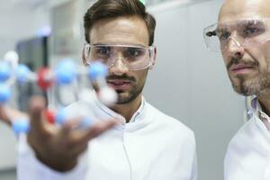 Confident male scientists analyzing molecular structure at illuminated laboratory photo