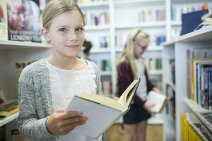Portrait of smiling schoolgirl with book in school library photo