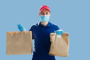 Delivery man in mask and gloves bring fresh food to customer's home. Stay home. Online shopping concept. blue background photo