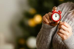 Woman holding red alarm clock near christmas tree photo