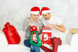 Pareja alegre cara cheque fuera regalo en Navidad calcetín. mujer y hombre en Papa Noel sombrero esperando regalo antecedentes. cheque contenido de Navidad media Navidad concepto. foto