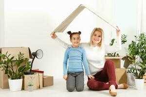 Cute mother and little daughter are on floor near boxes. They are preparing to move in another building. The parent and child are relaxing and smiling photo