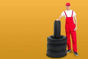 car mechanic carrying tire on yellow background. happy man smiling amd looking into camera photo