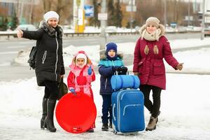 Family dressed in warm winter clothing walking down a quiet street in town with luggage in a travel and tourism concept photo