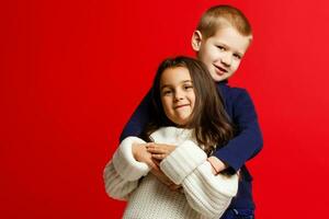 dos contento gracioso niños en pie juntos y abrazando, aislado en rojo foto