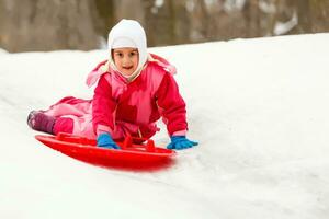 Cute little girl sliding down from the hill top covered with white and fluffy snow. One of the children favorite activity in winter time. photo