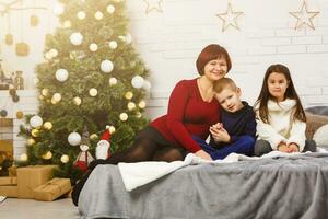 Family on Christmas eve at fireplace. Mother and little kids opening Xmas presents. Children with gift boxes. Living room with traditional fire place and decorated tree. Cozy winter evening at home. photo