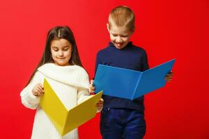 Two smiling school kids with colorful stationery, isolated on red background. School, education concept. photo