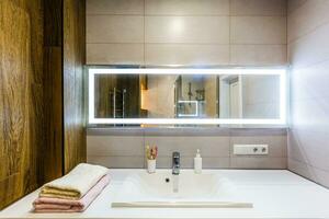 White and brown bathroom boasts a nook filled with double vanity cabinet topped with white and grey counter paired with tile backsplash under framed mirror photo