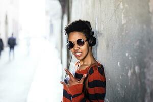 Portrait of young woman listening music with headphones showing Rock And Roll Sign photo