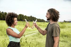 contento Pareja tintinamente cerveza botellas en el naturaleza foto