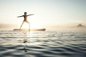 Woman practicing paddle board yoga on lake Kirchsee in the morning, Bad Toelz, Bavaria, Germany photo