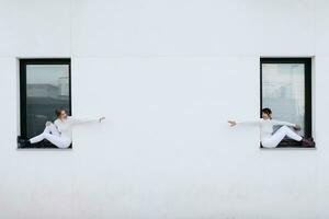 Young women sitting on windows with arms outstretched towards each other during COVID-19 photo