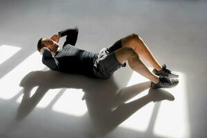 Athlete doing crunshes in sunlit studio photo