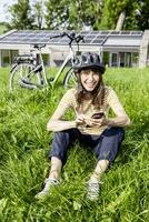 Laughing woman with bicycle using cell phone on a meadow in front of a house photo